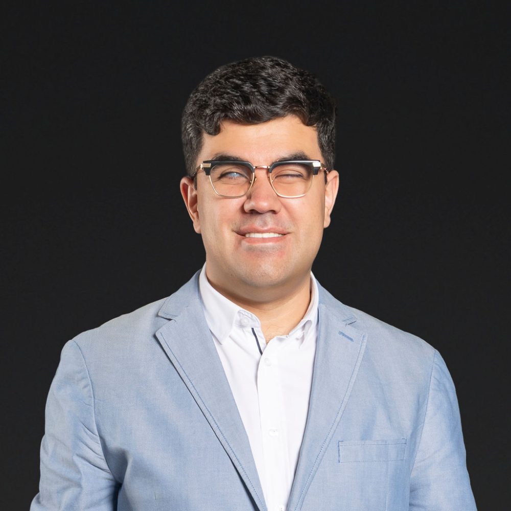 Headshot of Santiago Velasquez smiling against a dark background.