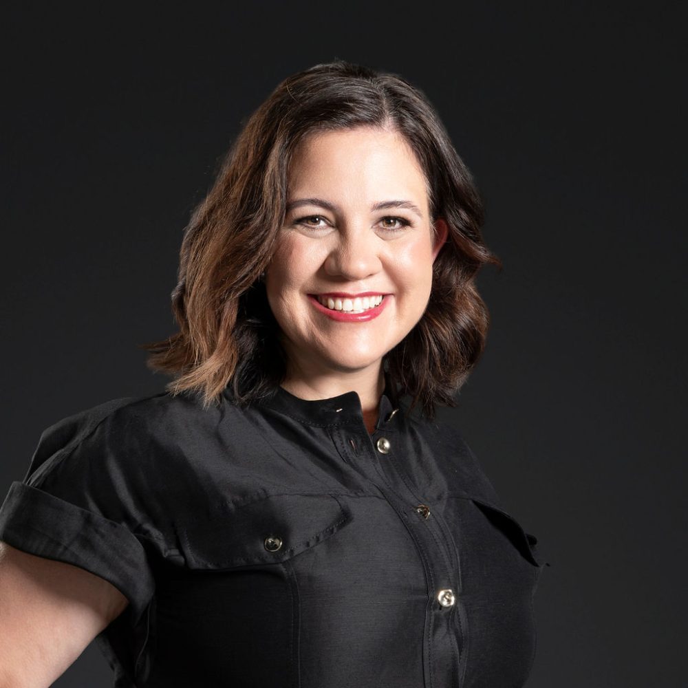 Headshot of Kate Fisher smiling against a dark background.