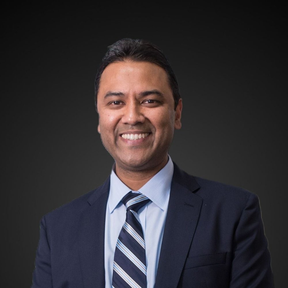 Headshot of Rolf Gomes smiling against a dark background.